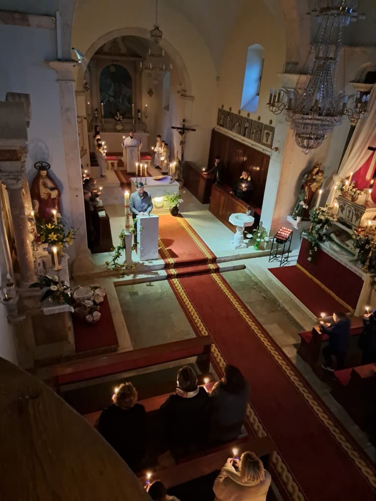 Vjernici stoje u klupama i drže upaljene svijeće