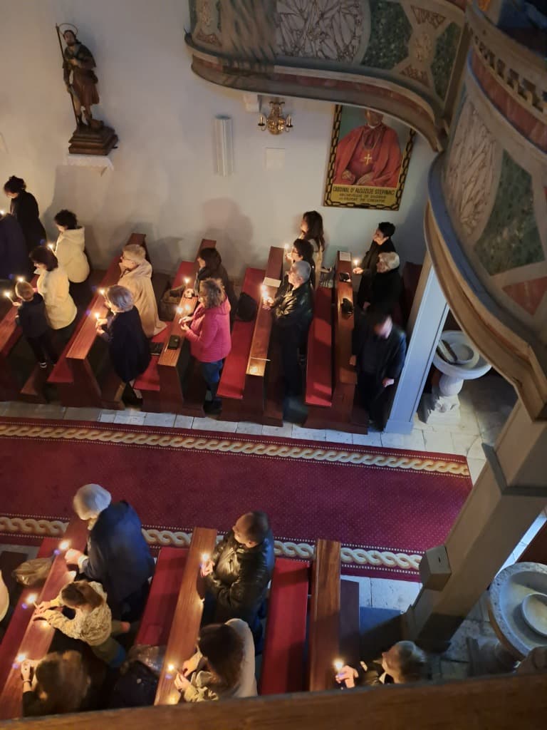 Pogled s pjevališta na vjernike u crkvi s upaljenim svijećama