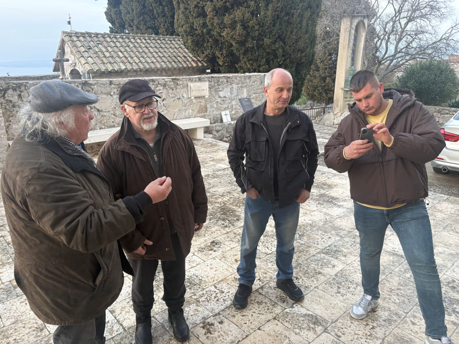 Barba Stipe objašnjava viziju novih vrata župljanima na trgu ispred crkve